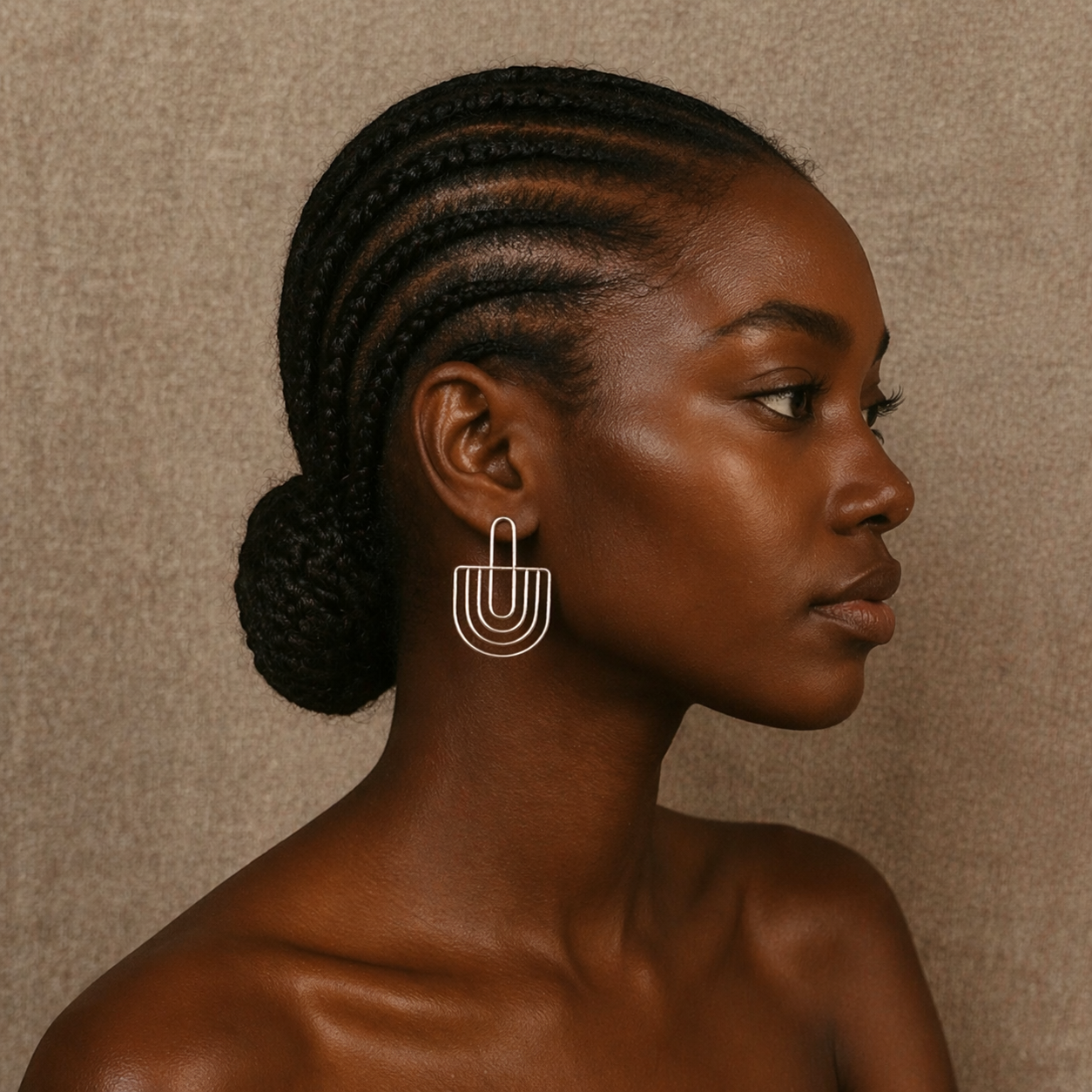 Woman with braided hair wearing a modern earring against a neutral background