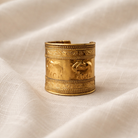 Gold bracelet with intricate designs on a beige fabric background