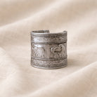 Silver bracelet with embossed designs on a beige fabric background