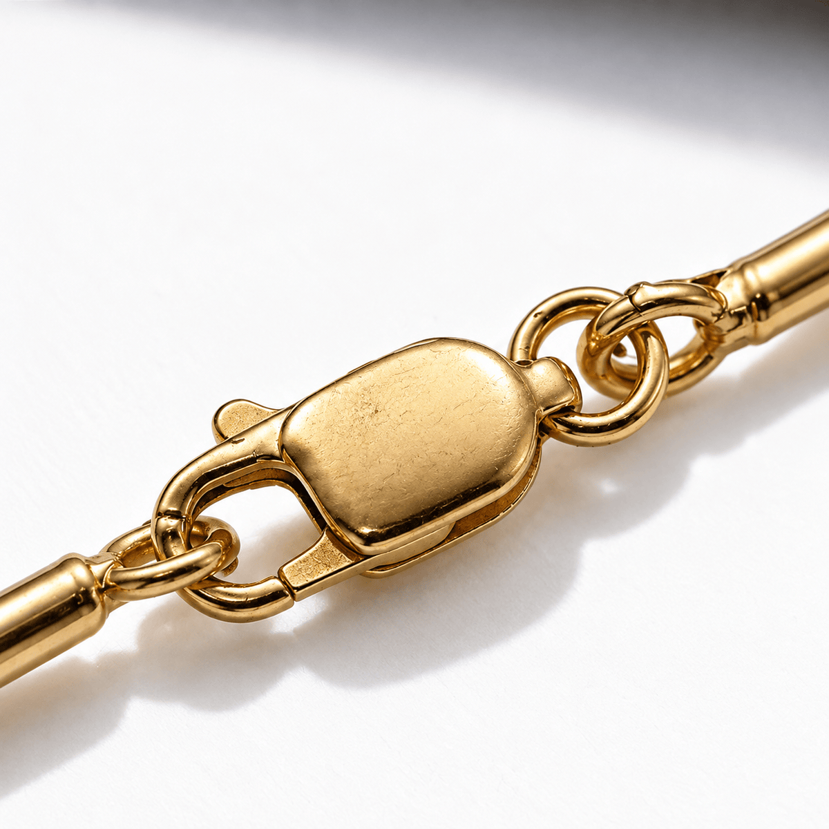 Close-up of a polished yellow gold chain bracelet showing a lobster clasp and ring connector on a white background.